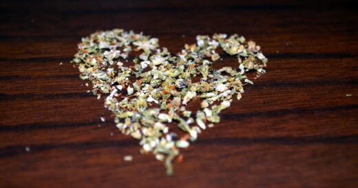 cannabis flower arranged in the shape of a heart on a brown wooden surface.