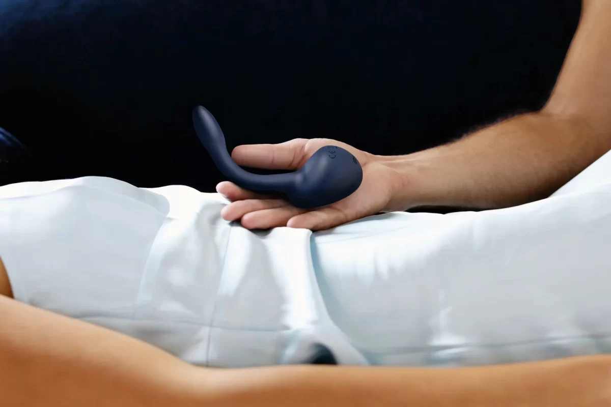 A man's hand holds the prostate vibrator the MysteryVibe Molto above a woman's pelvis.