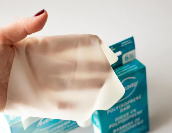A hand holds a Harmony Polyisoprene Non Latex Dental Dams for oral sex in front of its packaging.