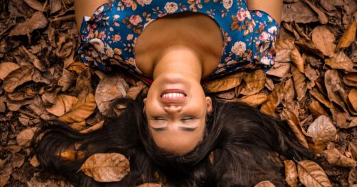 Woman smiling lying back on leaves with eyes closed.