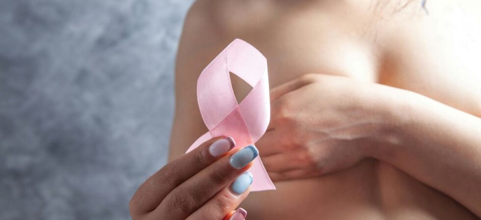 woman holds a pink ribbon while covering her breasts signifying sex after breast cancer