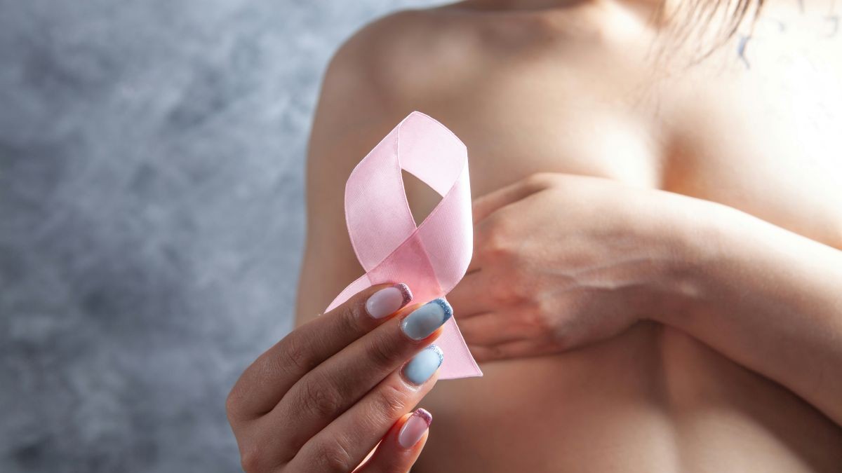 woman holds a pink ribbon while covering her breasts signifying sex after breast cancer