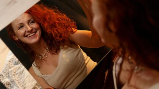 woman with red hair looking into a mirror she is holding
