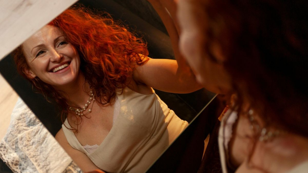 woman with red hair looking into a mirror she is holding